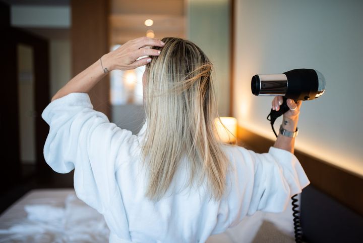 A woman seen from behind drying her long hair with a hair dryer