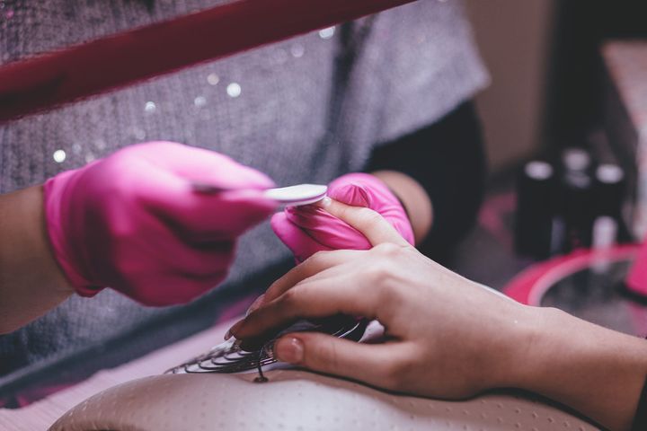 A nail technician in pink gloves filing a client’s nails