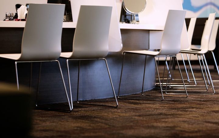 A row of white chairs at a salon counter with a round mirror